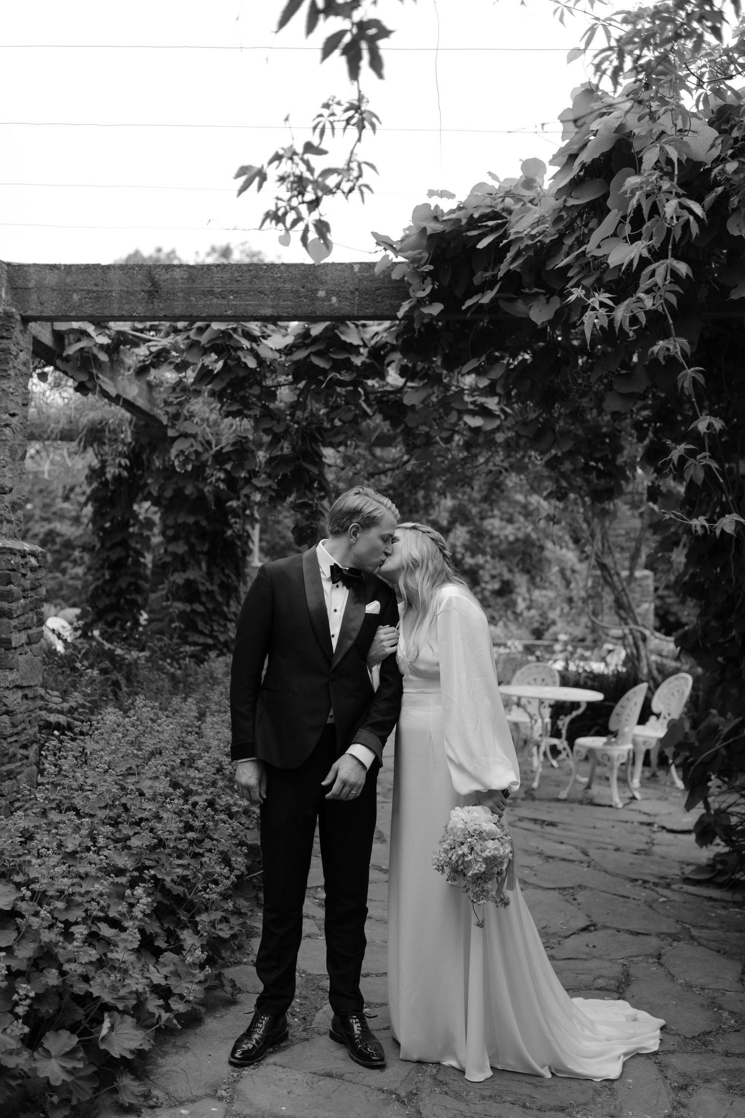 Romantic wedding couple sharing a tender moment under an ivy-covered garden arch.