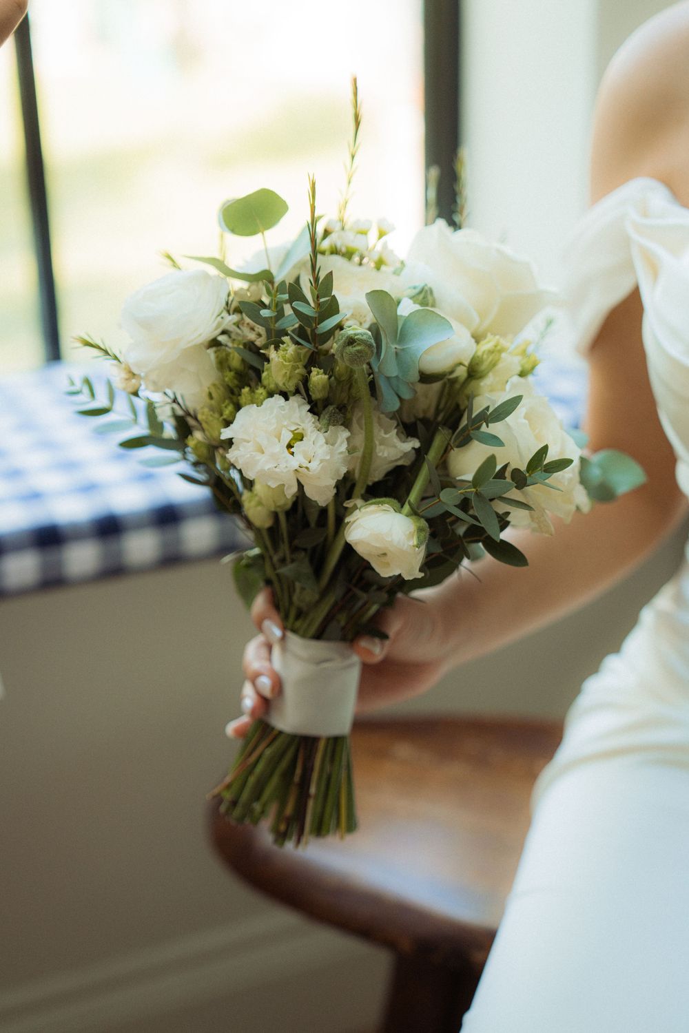 Bride holds elegant white and green wedding bouquet with roses and eucalyptus greenery.