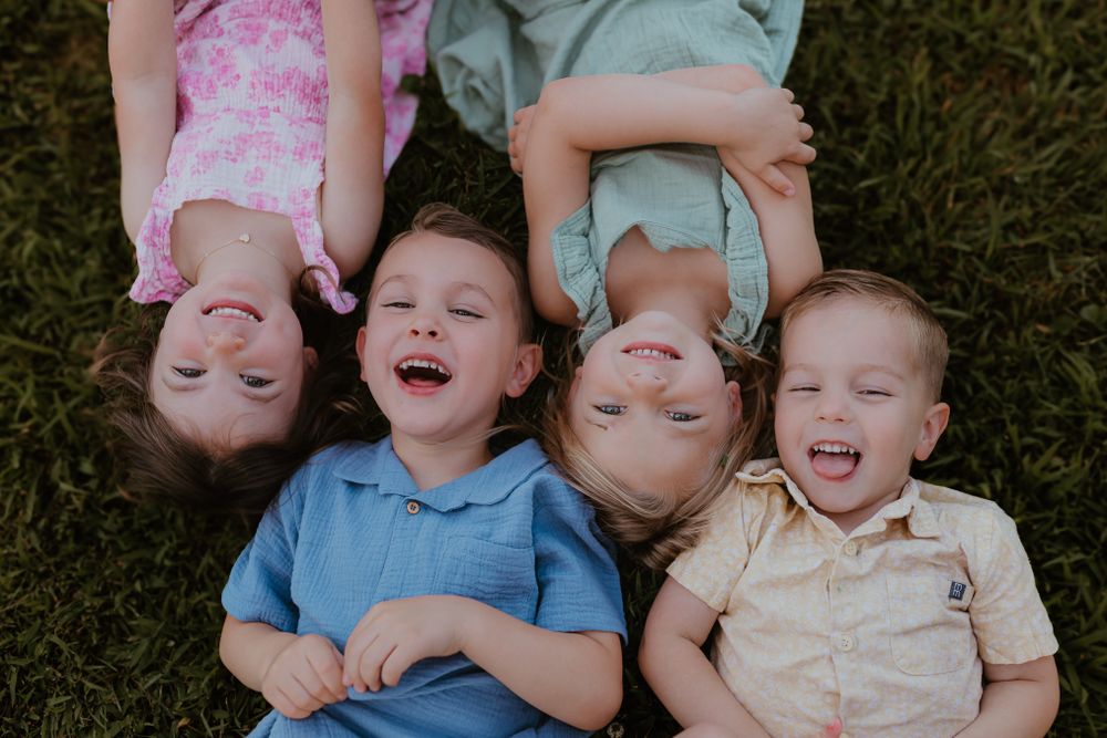 Four children lying on grass in a circle formation, laughing and smiling at the camera. Colorado Springs Photographer.
