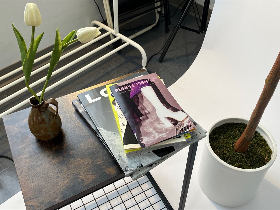 Stylish desk arrangement with magazines, white tulips in vase and potted plant.