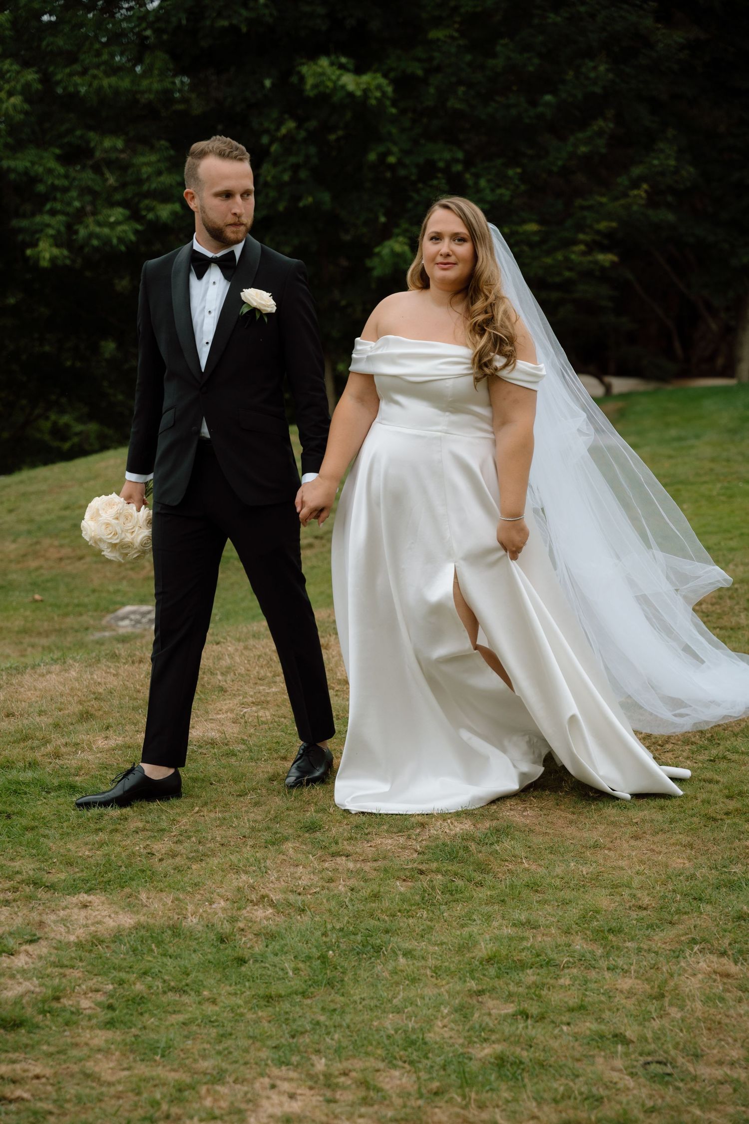 A wedding couple poses for photos on a grassy hill overlooking a serene lake.