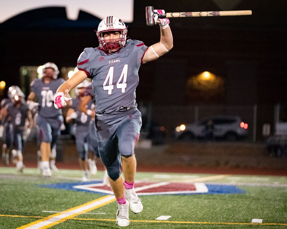 Football player in grey uniform celebrates on field while holding up equipment.