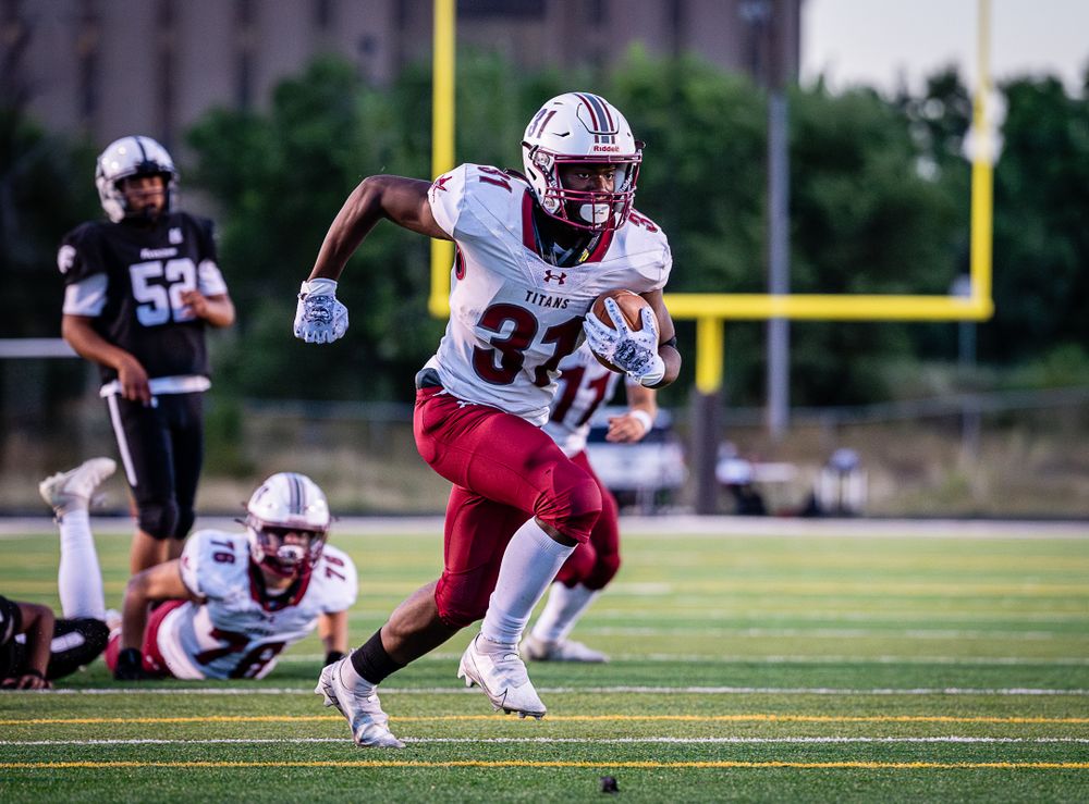Running back in maroon uniform sprints down field during football game.