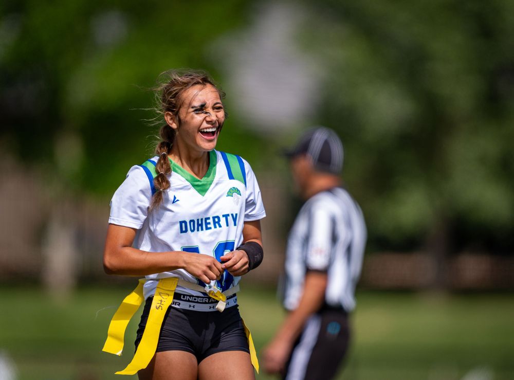 Flag football player smiles during sunny outdoor game.