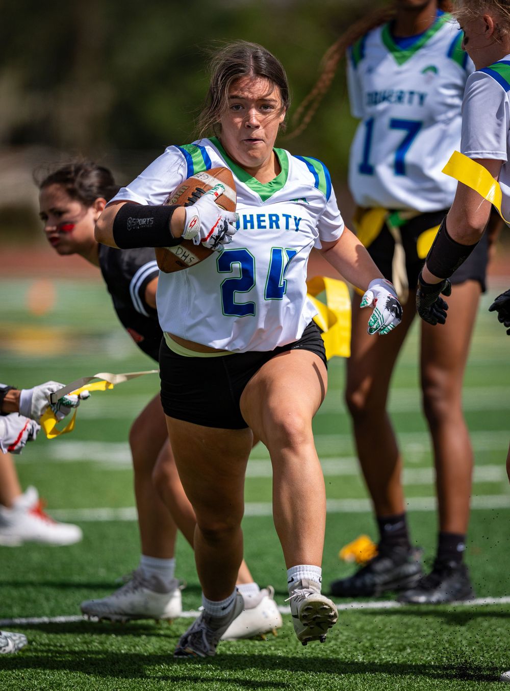 Flag football player in Liberty jersey carries ball while dodging defenders.
