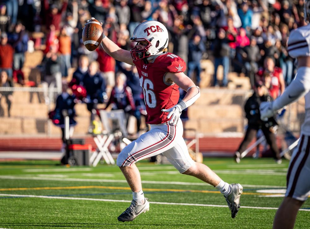 Football player in red jersey runs with ball raised during game play.