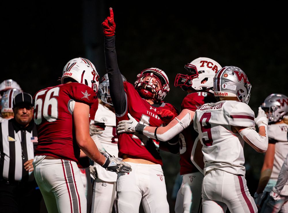 Football players celebrate during night game with referee in background.