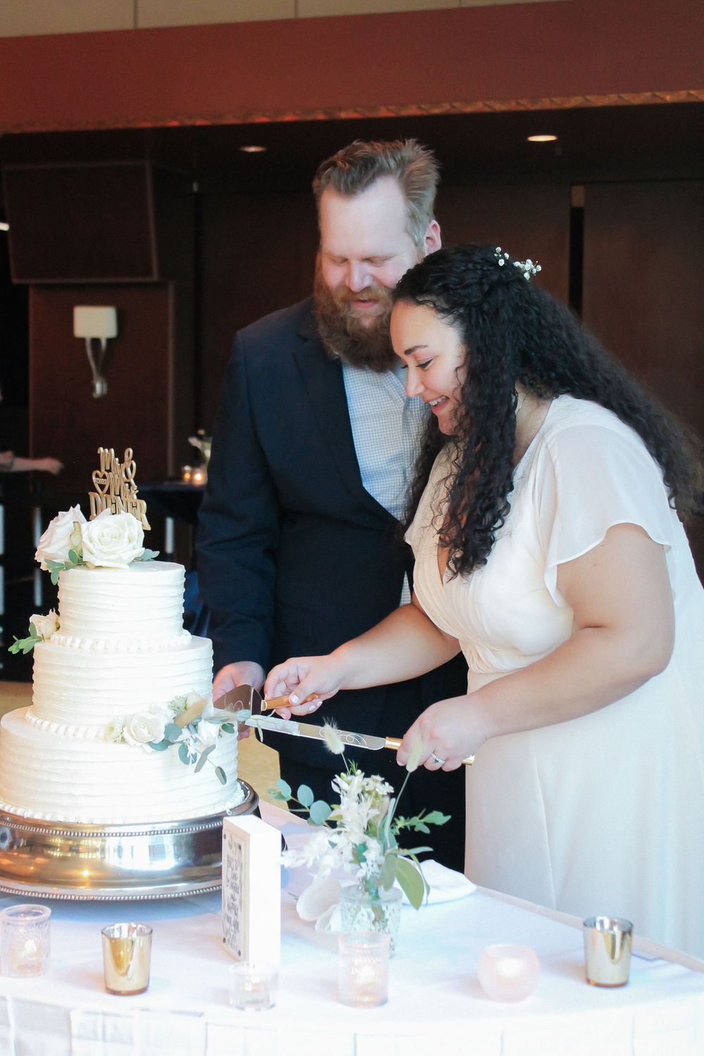 Couple cutting their elegant white wedding cake decorated with greenery.