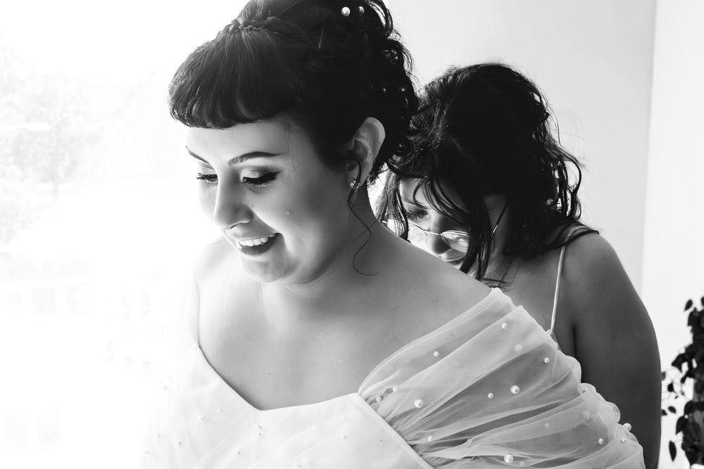 A black and white photo of a bride smiling while getting ready for her wedding ceremony.