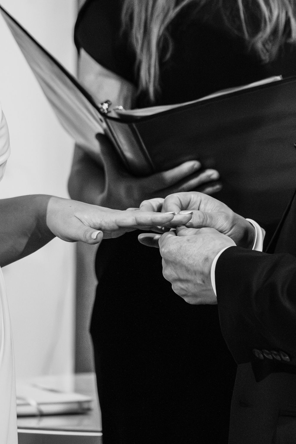 Black and white photo of hands exchanging rings during a wedding ceremony.
