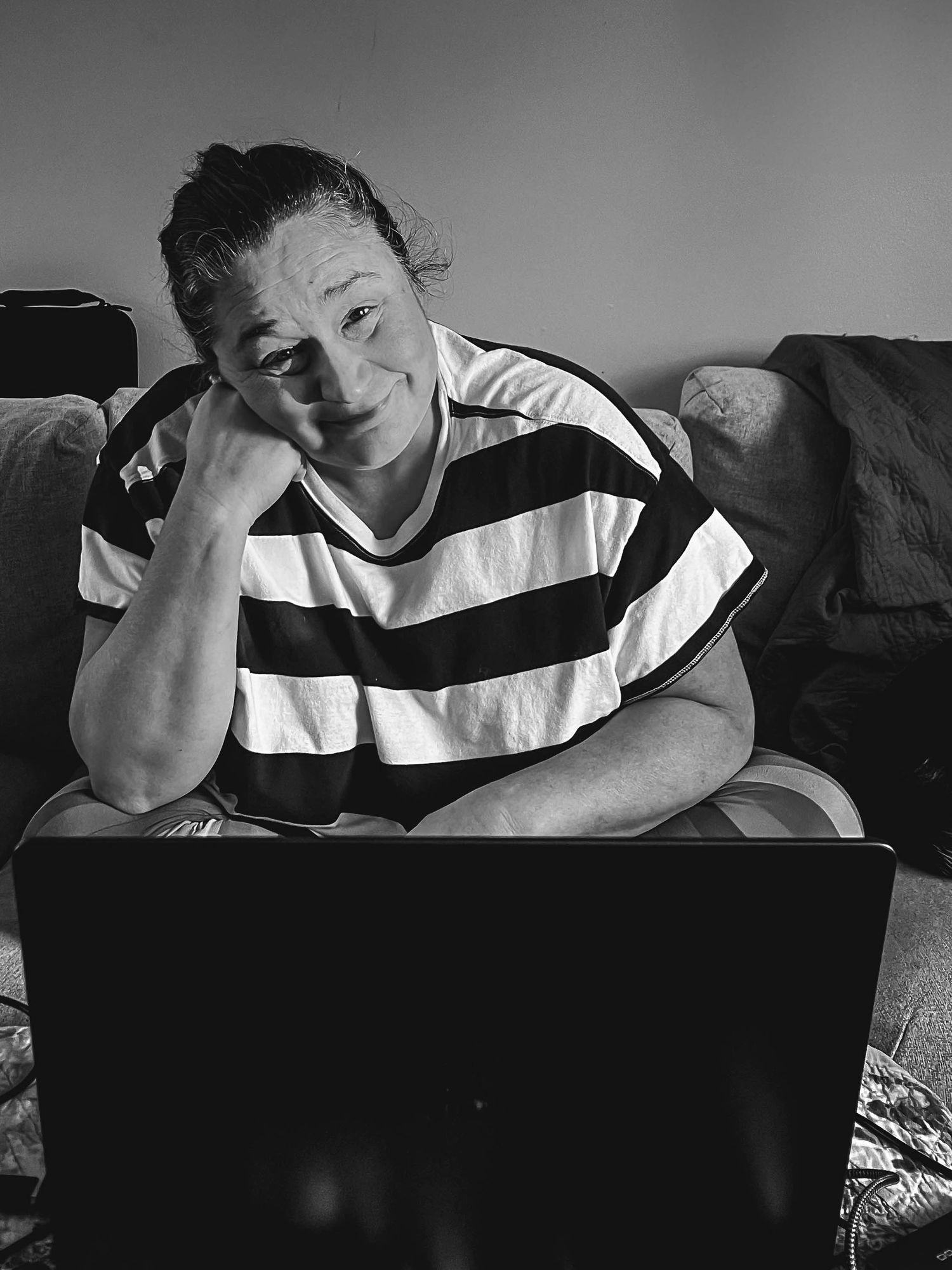 A person in a black and white striped shirt sits casually on a couch while looking at a laptop.