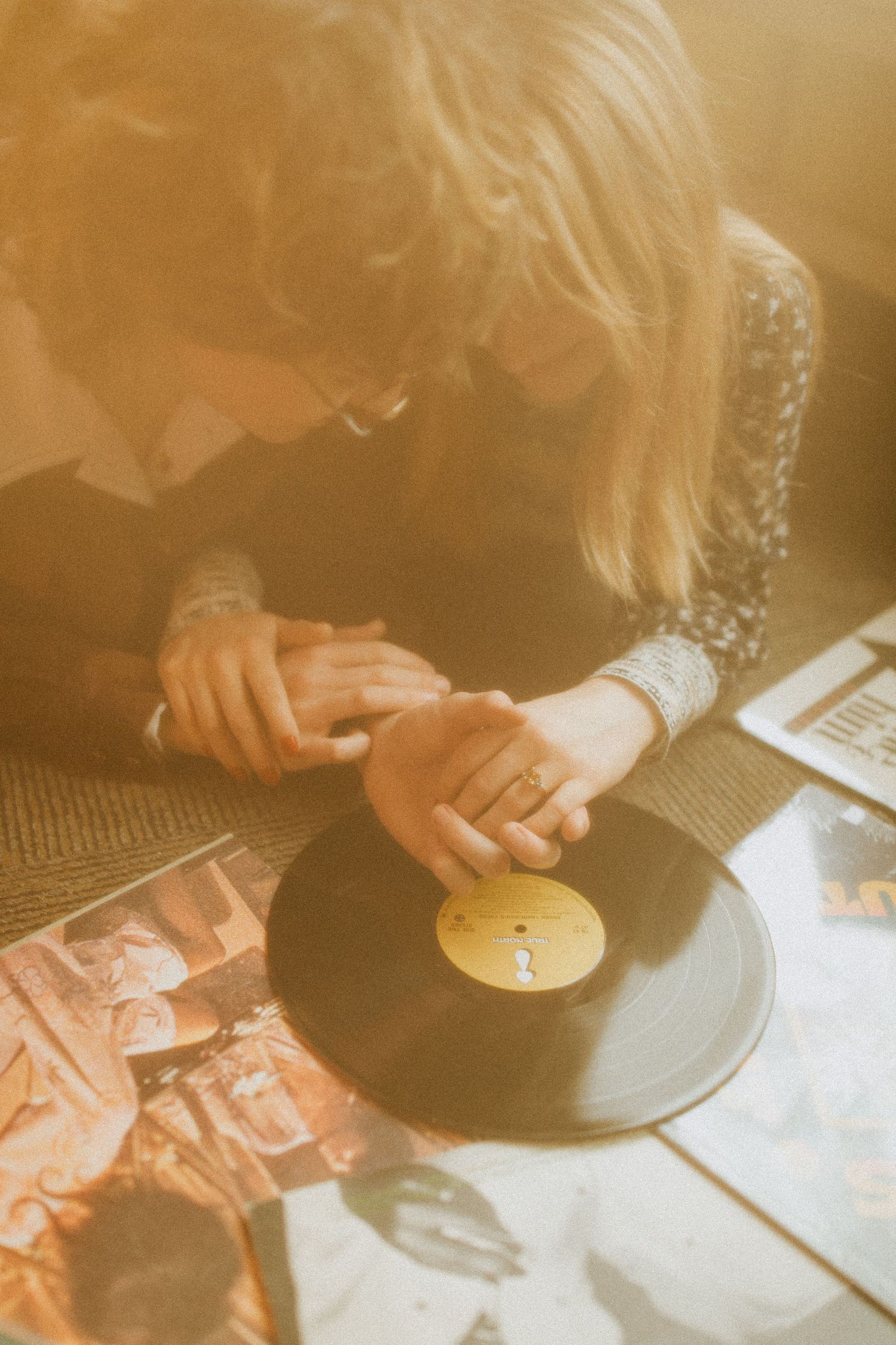 Hands gently holding vinyl record with scattered album covers visible.