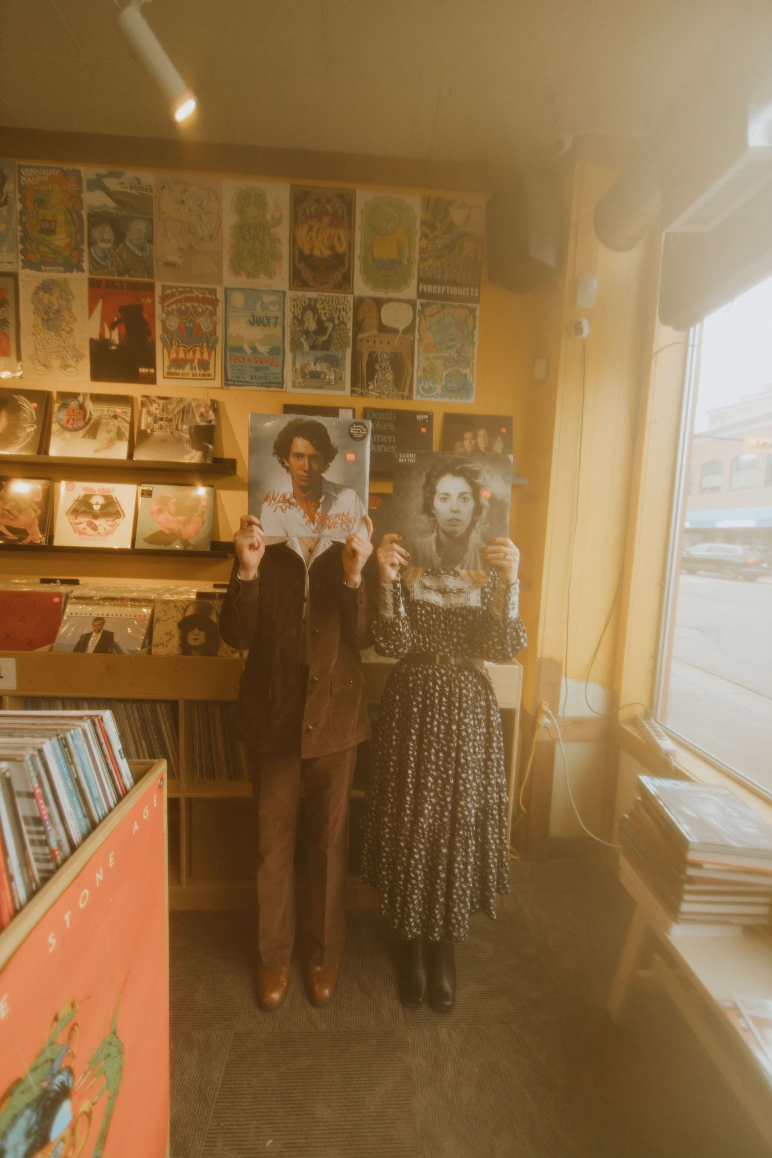 Two people pose together in a record store with vintage posters and album covers displayed on the walls.