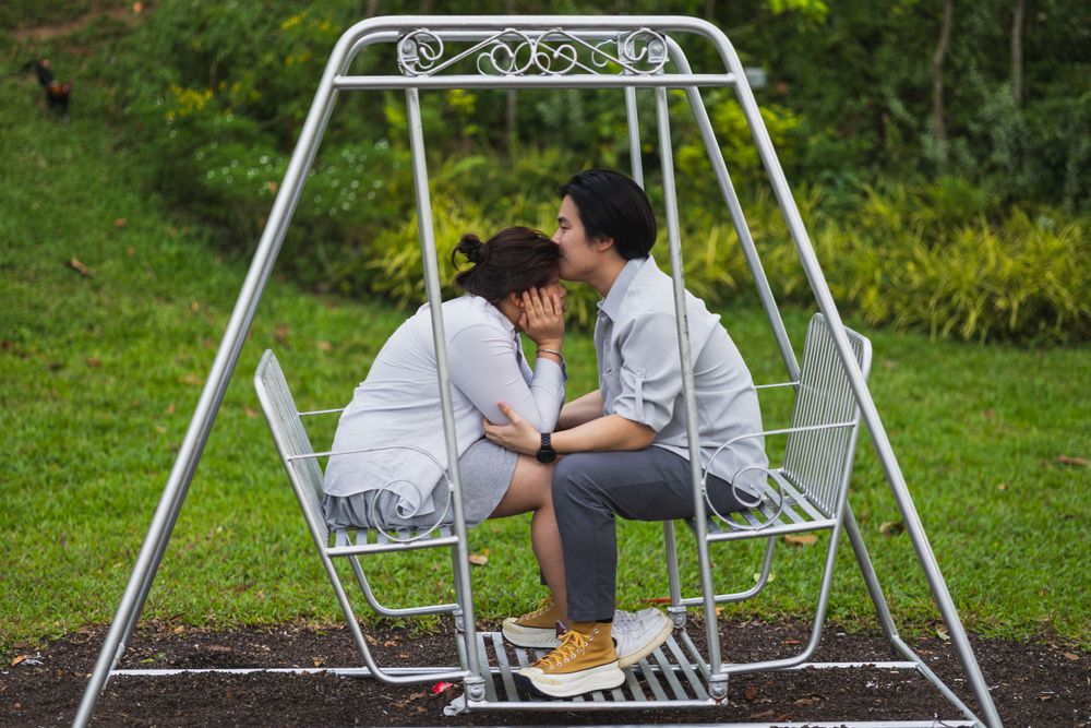 Two people share a quiet moment on a metal garden swing surrounded by greenery.