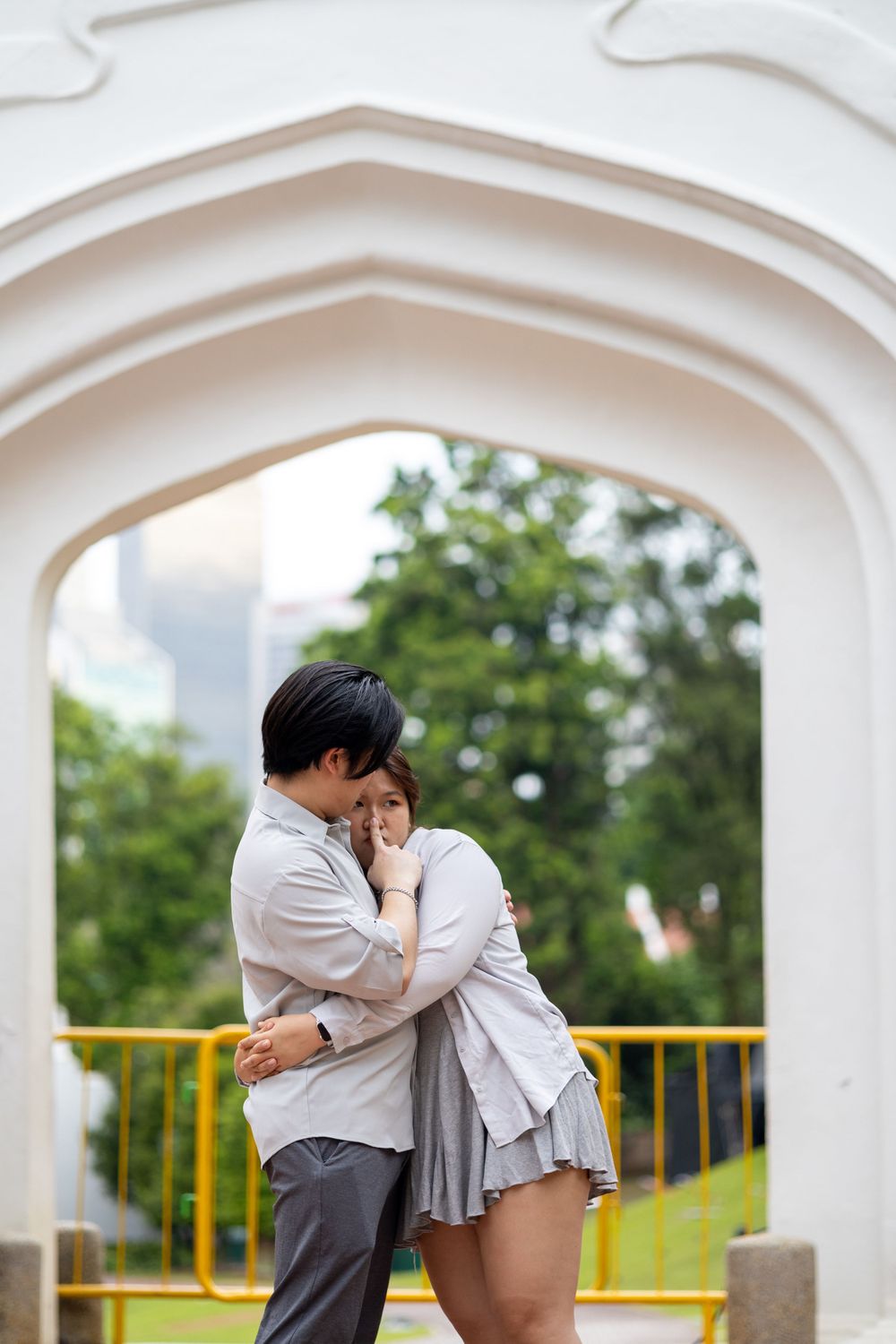 A tender embrace captured under a white Gothic arch in a park setting.
