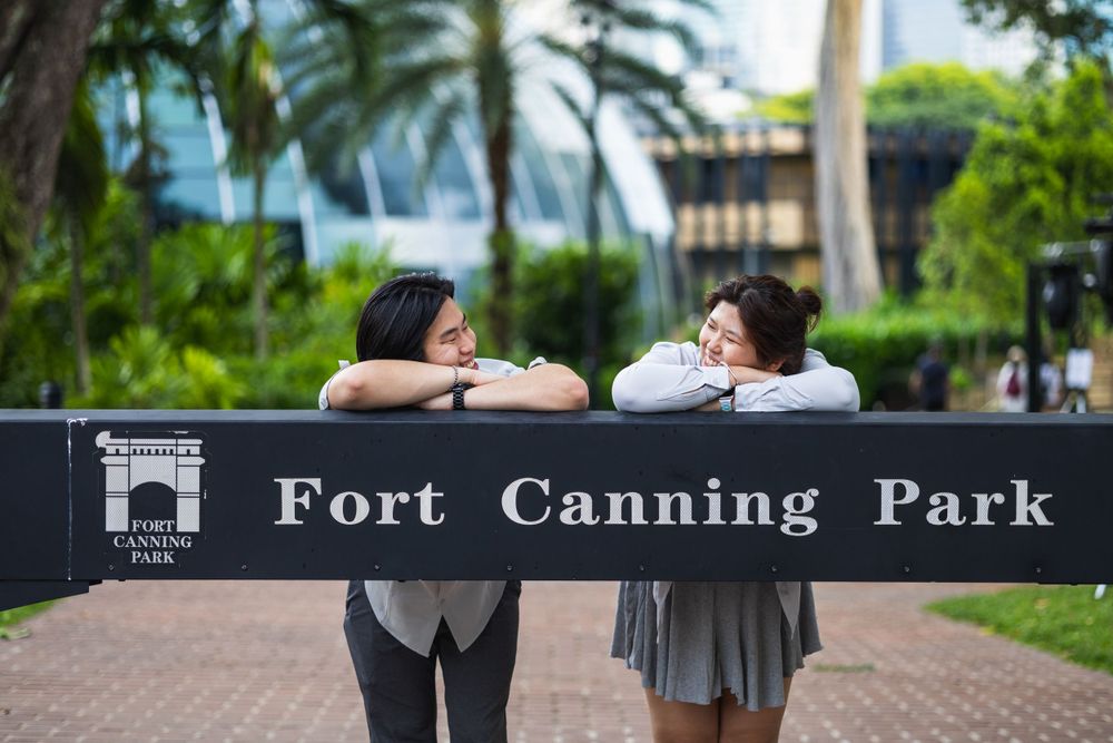 Two people sharing a casual moment while leaning on a sign at Fort Canning Park.