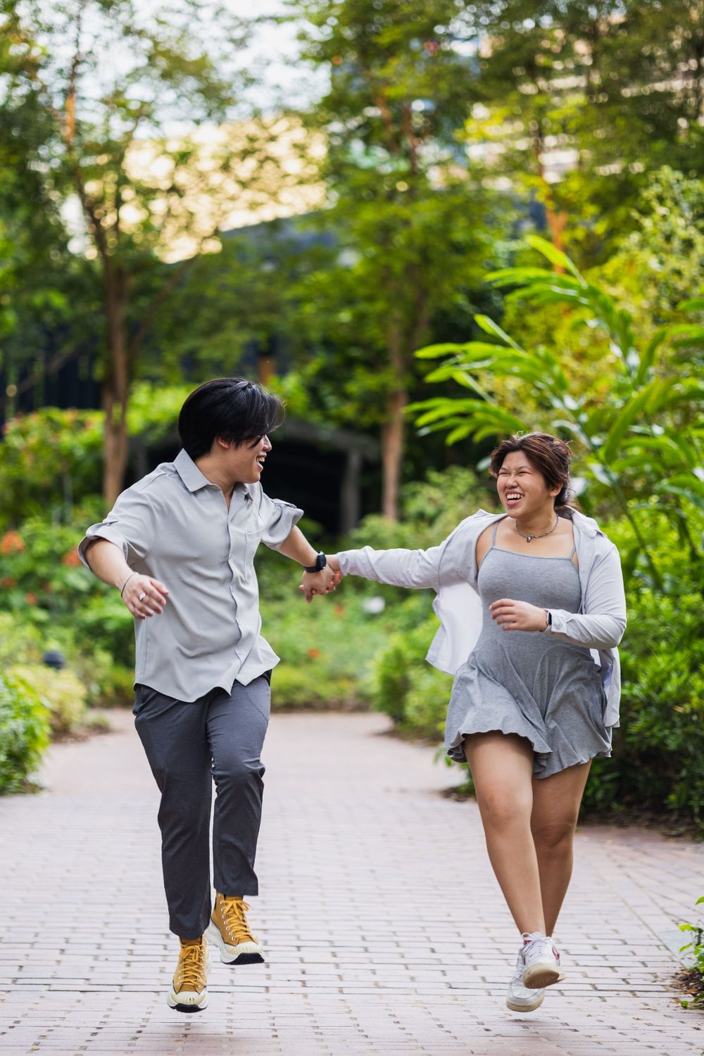 Two people run playfully through a lush garden path on a sunny afternoon.