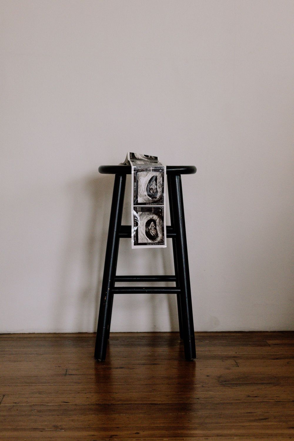 Two black and white photographs arranged on a minimalist black wooden stool against a neutral wall and hardwood floor.