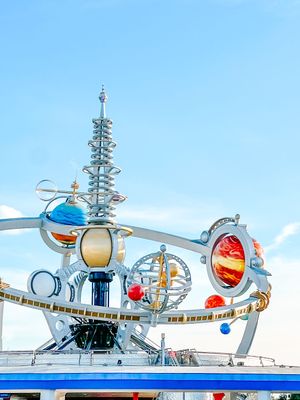 A futuristic silver and white amusement park attraction with retro-space design elements against a bright blue sky.