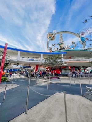 A panoramic view of Disneyland's Tomorrowland entrance with blue skies and crowds of visitors on a sunny day.