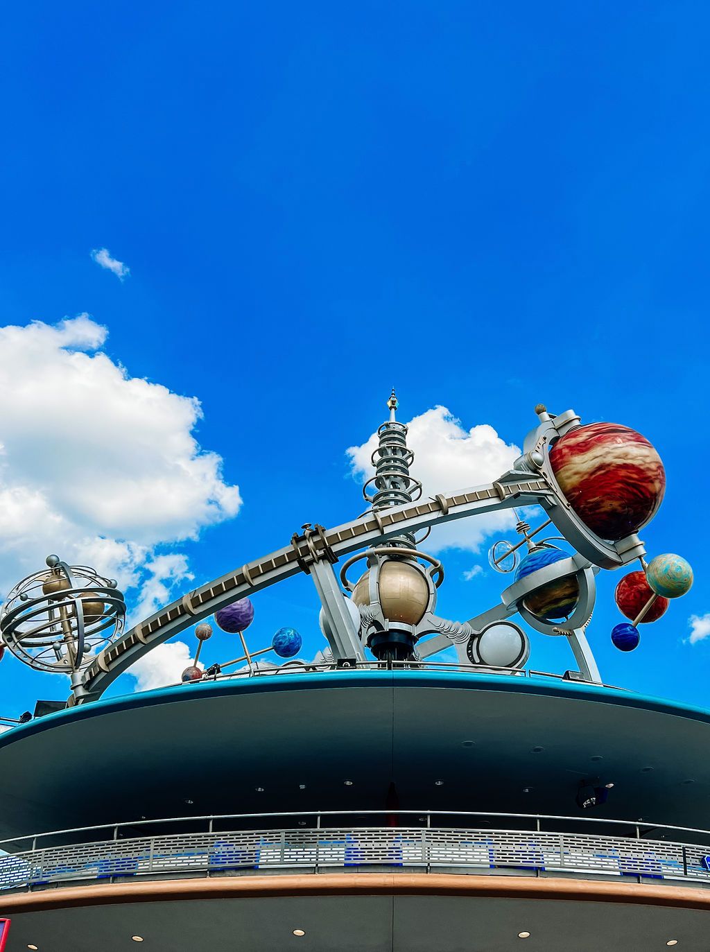Futuristic space-themed ride structure with colorful orbs and planets against bright blue sky at Tomorrowland in Disney park.