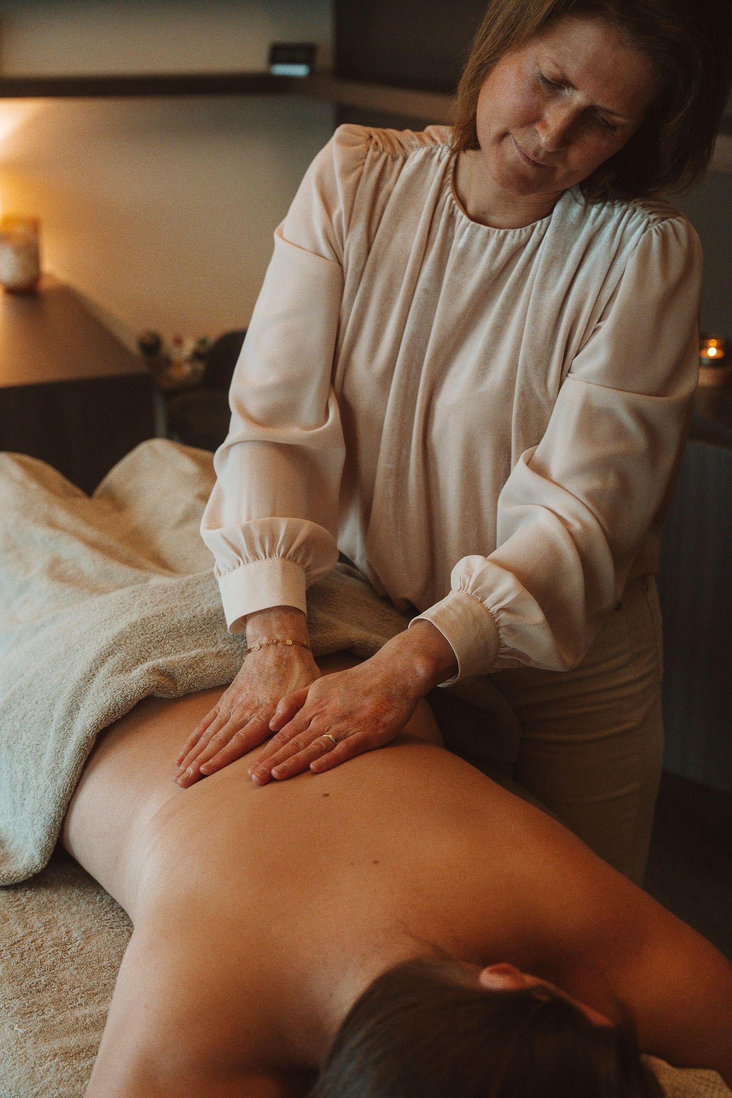 Massage therapist performing relaxing back massage treatment in dim spa room with candlelight.