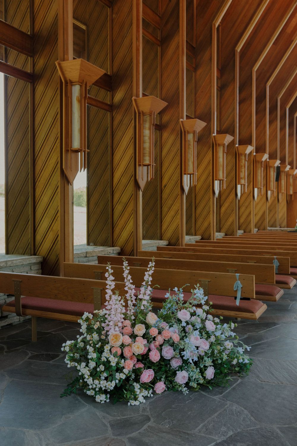 Soft pink and white floral arrangements decorate a wooden church interior.