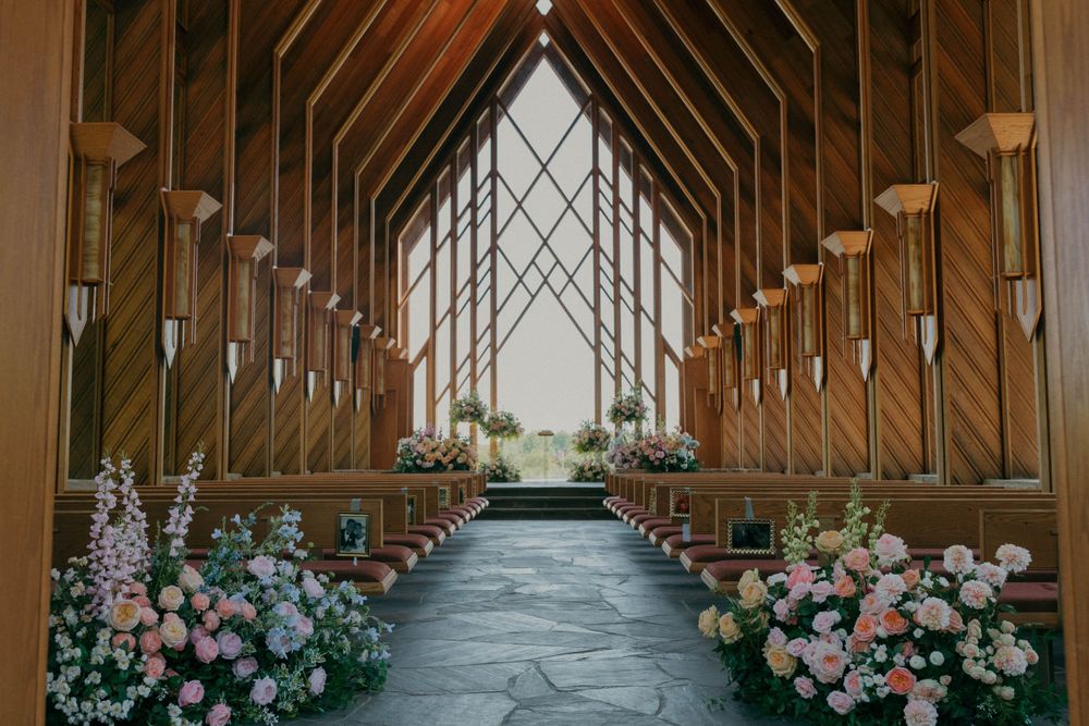 Wooden chapel interior with dramatic vaulted ceiling and floral arrangements lining the aisle.