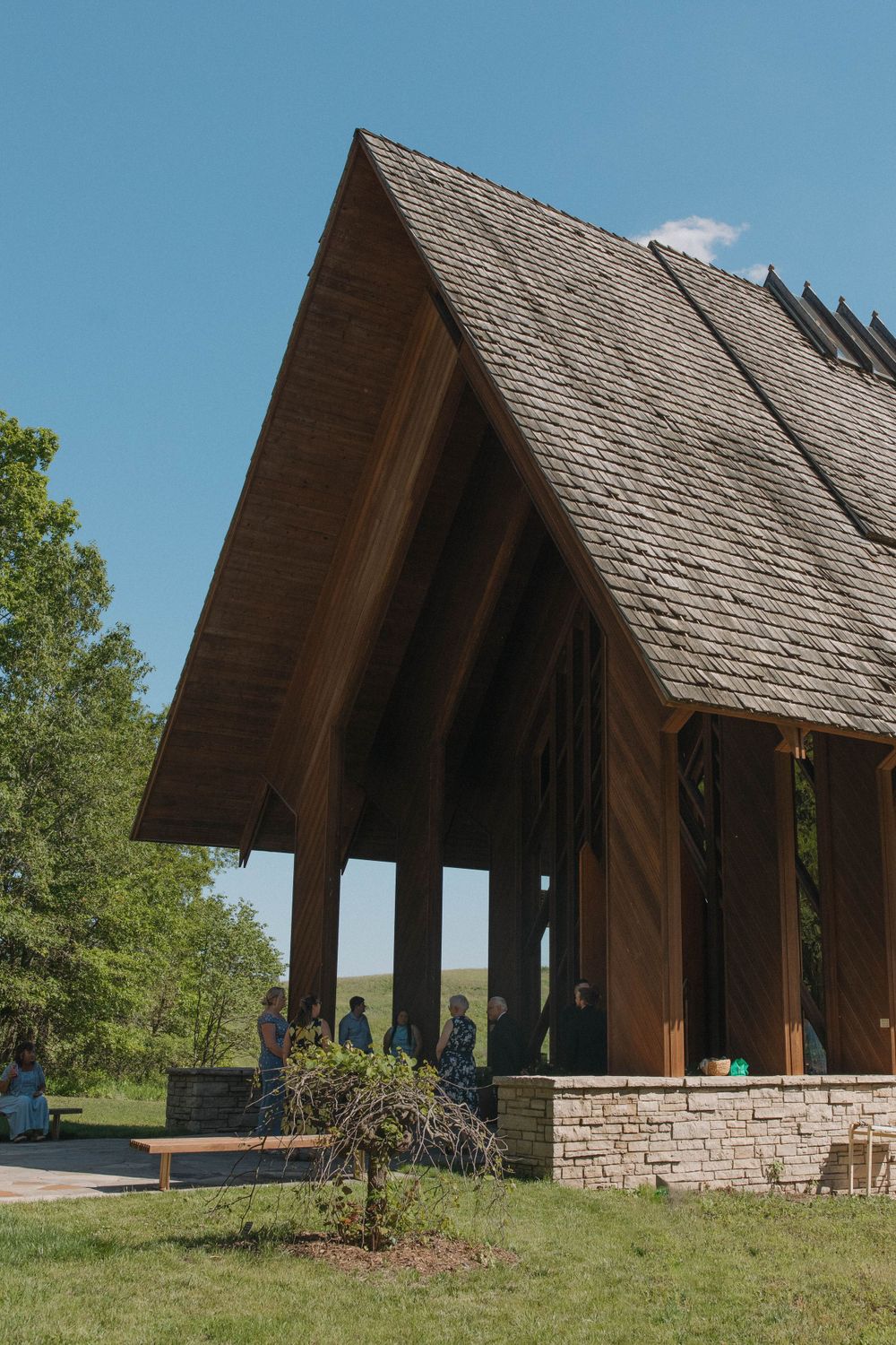 Modern wooden chapel with stone foundation and steep pitched roof in a pastoral setting.