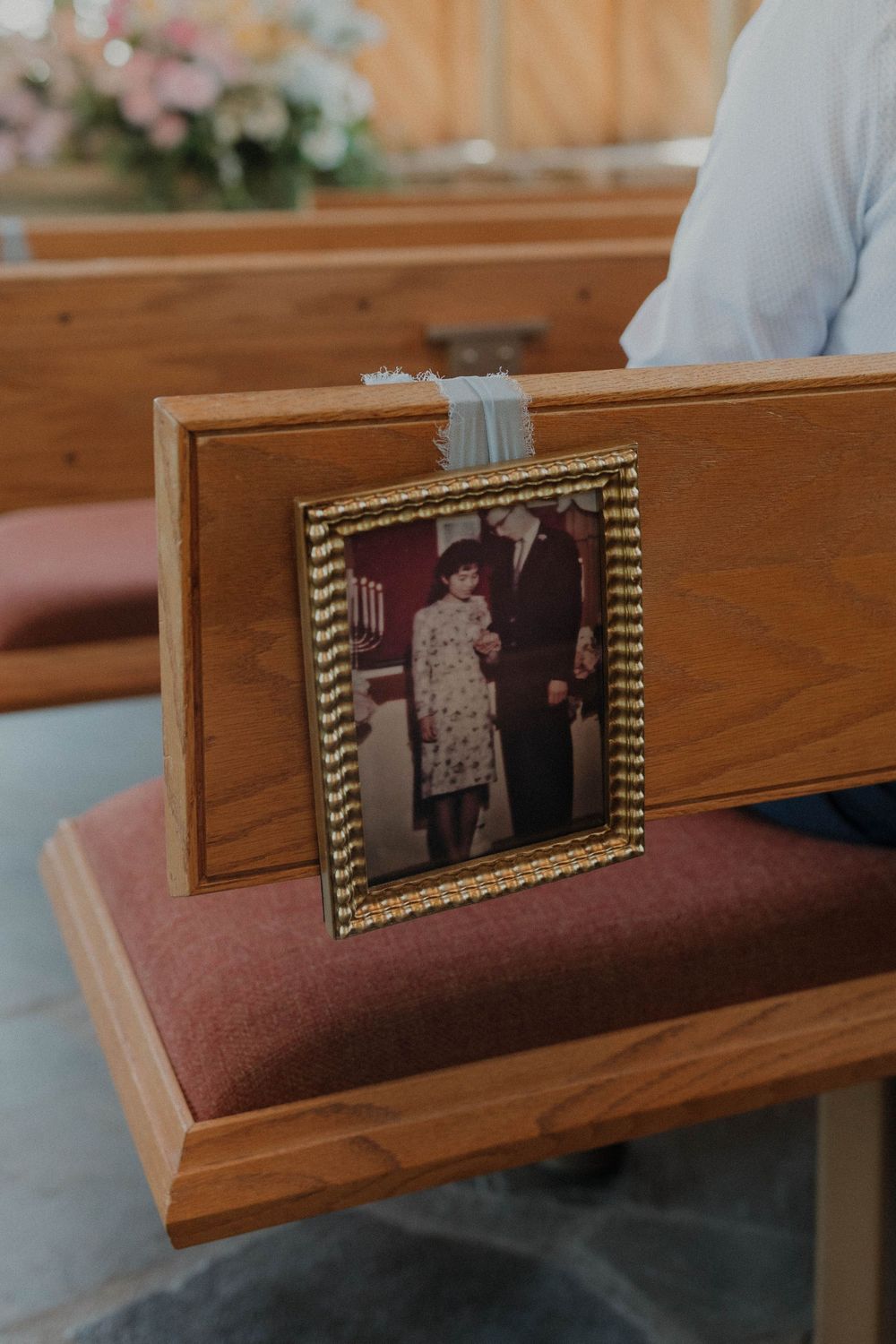 Vintage framed photograph displayed on wooden church pew with pink cushioning.