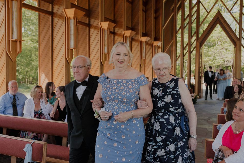 Wedding guests in formal attire seated in wooden church pews during ceremony.
