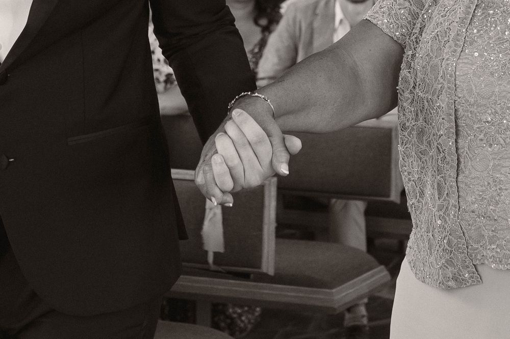Black and white close-up of joined hands during wedding ceremony.