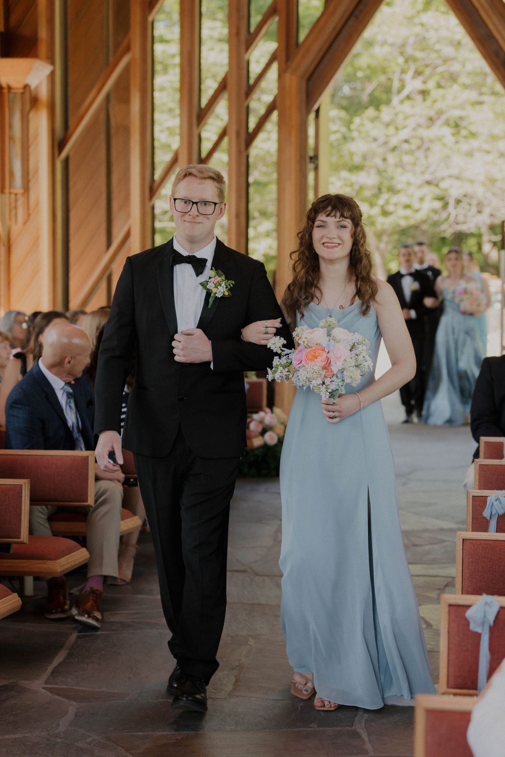 Wedding party members walking down church aisle with floral bouquet.