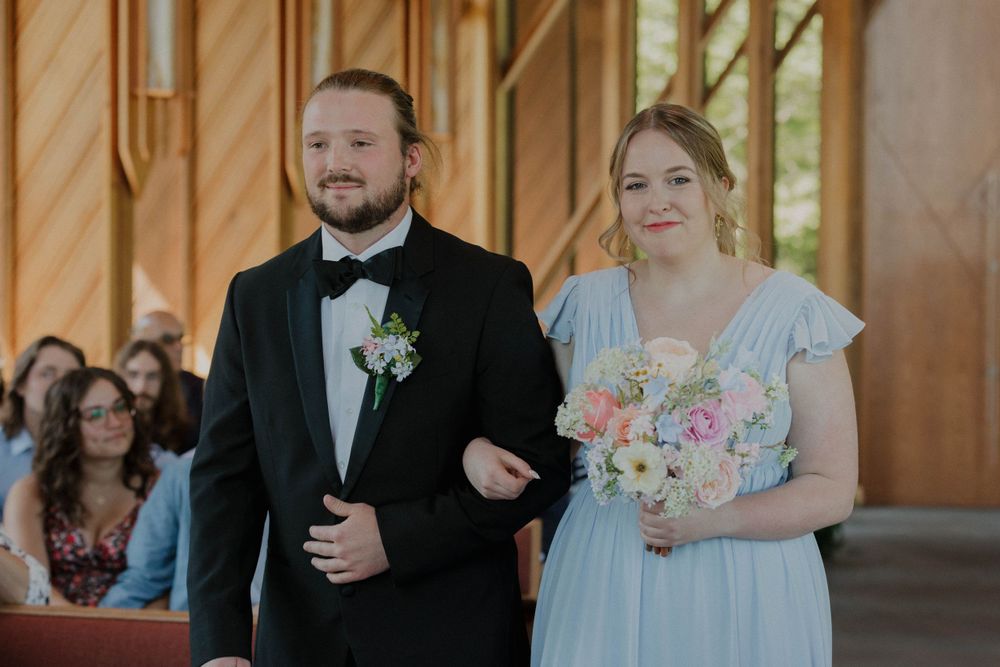 Wedding party members walking down church aisle with pastel bouquet.