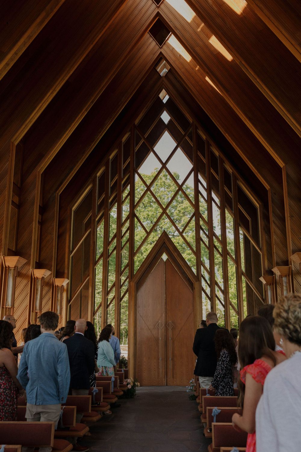 Interior of wooden chapel with dramatic angular beams and diamond-shaped window at altar.