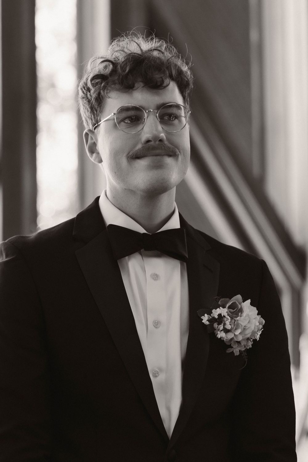 A close-up shot of a groom in a black tuxedo and bow tie with a white boutonniere.