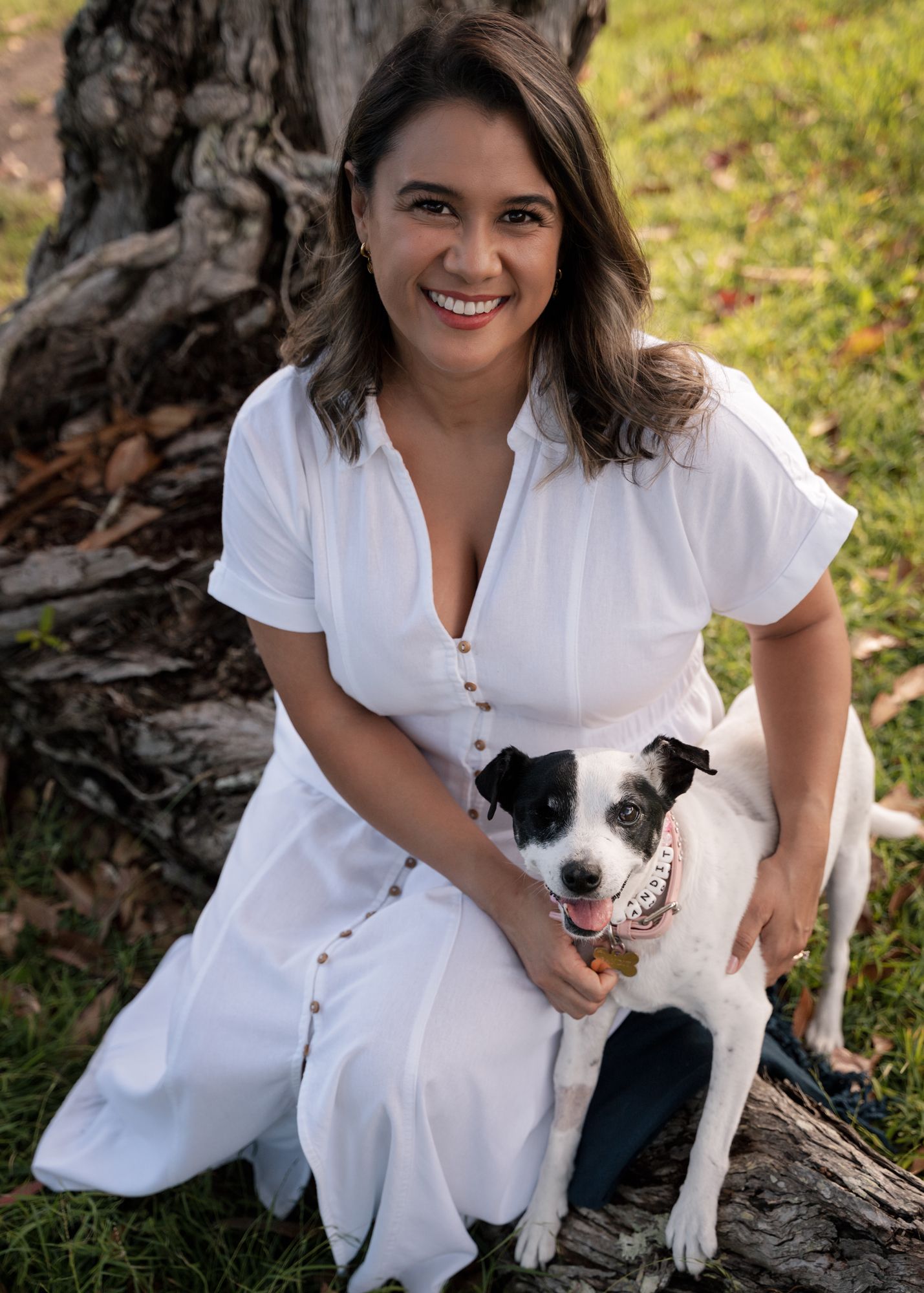 women sitting on a trunk hugging her dog and smiling towards the camera during her professional photoshoot in Sydney Lilli Pilli Reserve