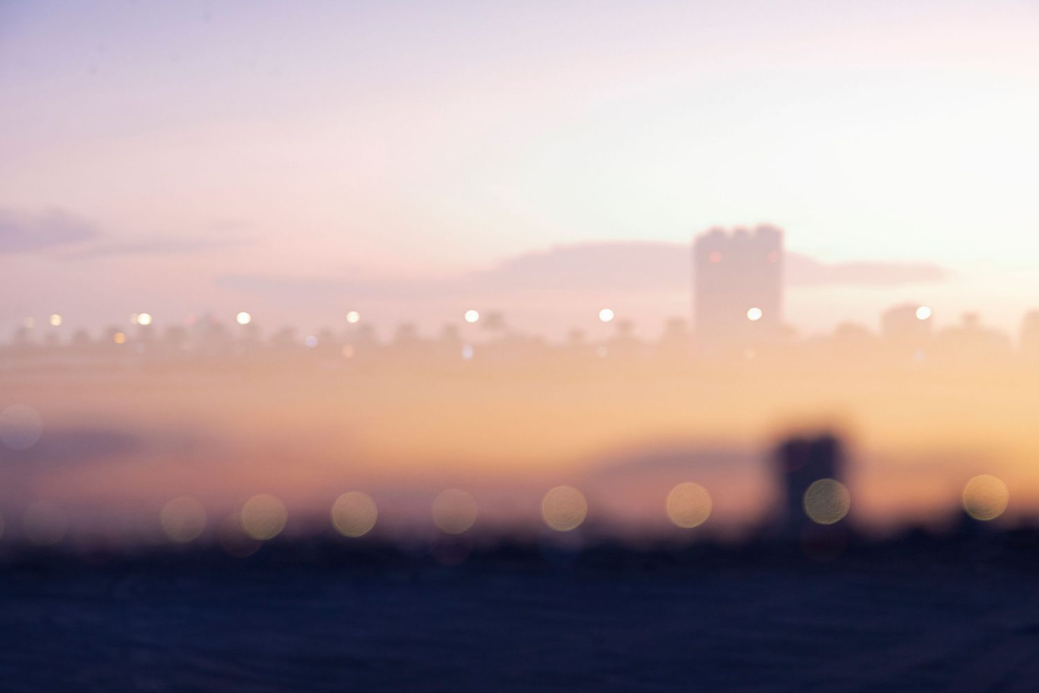 Dreamy cityscape bokeh with buildings silhouetted in misty golden sunrise light.