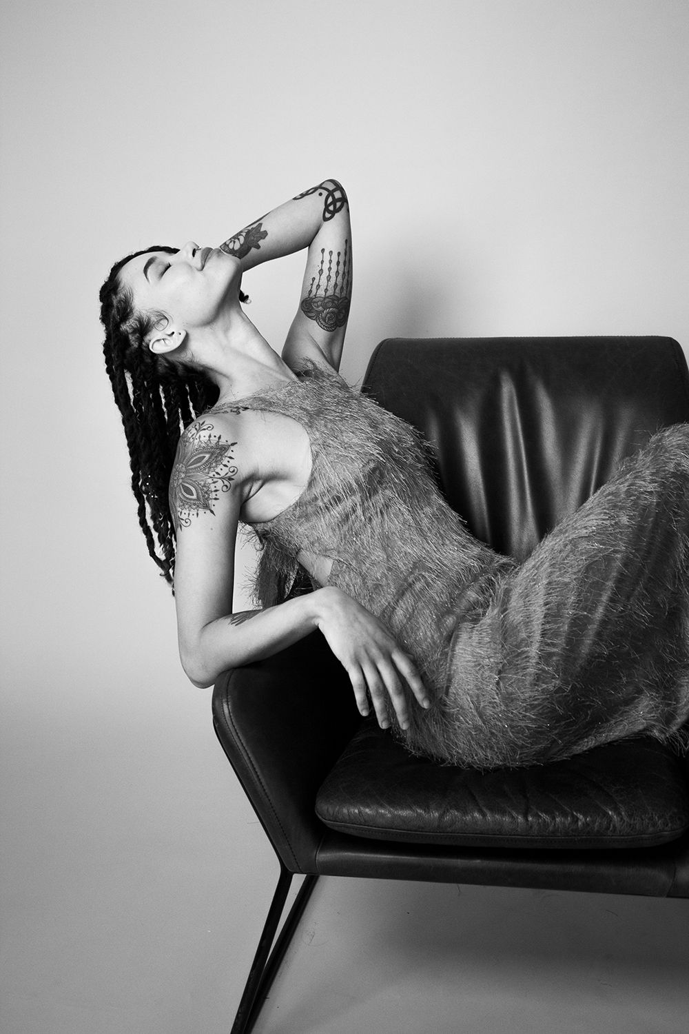 Artistic black and white portrait of model reclining on leather chair. Head back.