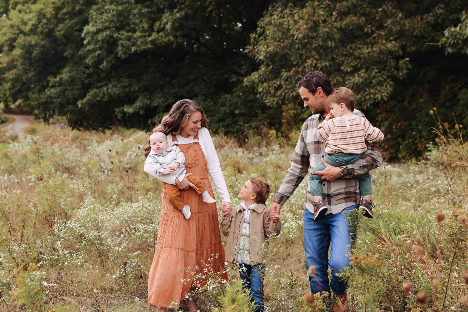 A family walks together through a sunny wildflower meadow on an autumn afternoon.
