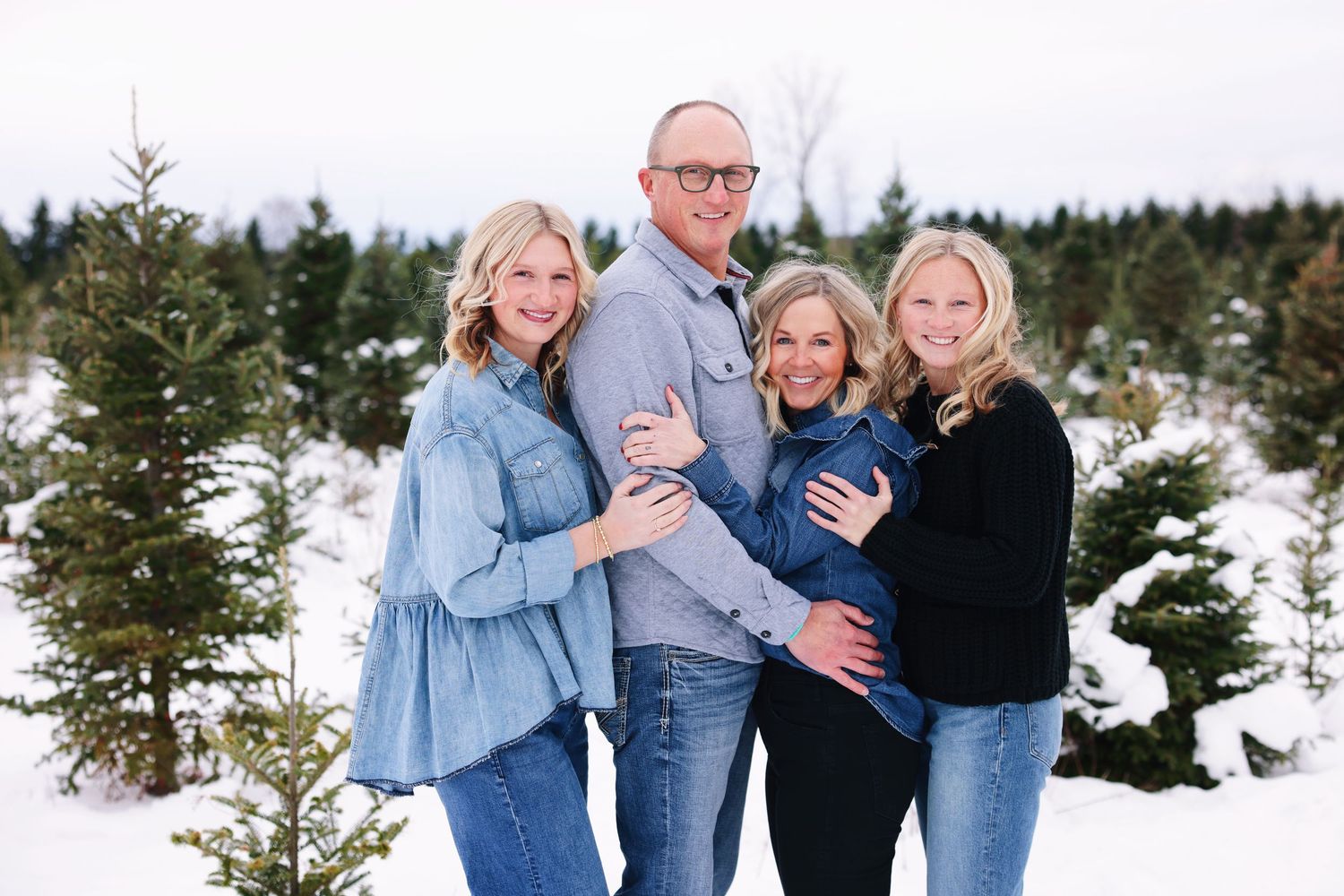A group enjoying winter photos in a snowy evergreen forest setting wearing coordinated blue and black outfits.