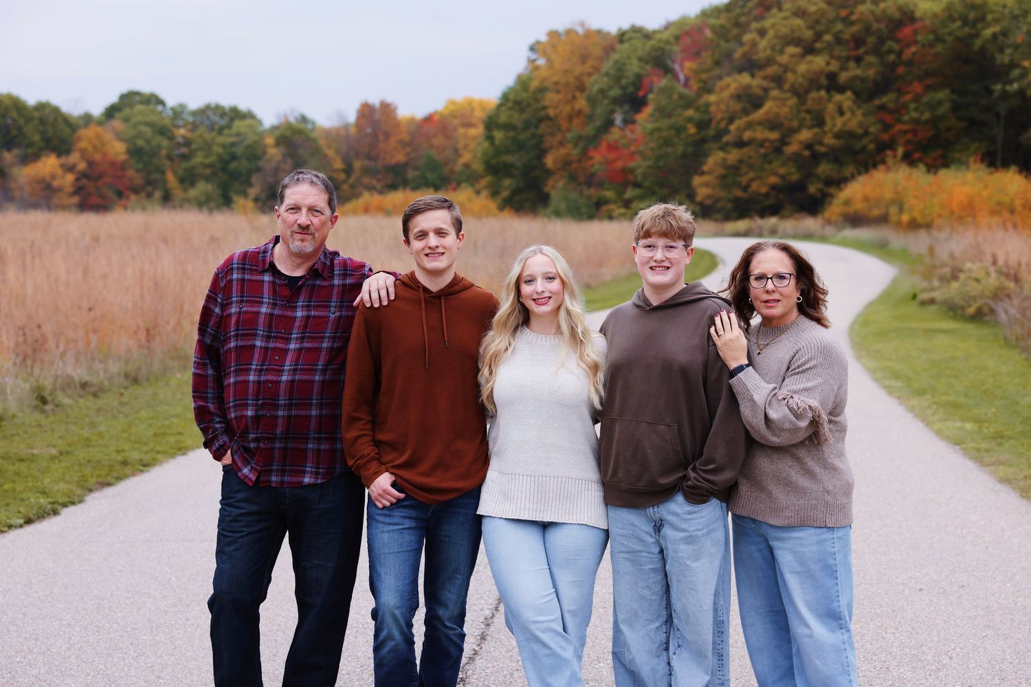 A group of people walking together on a gravel path surrounded by autumn foliage and tall grass.