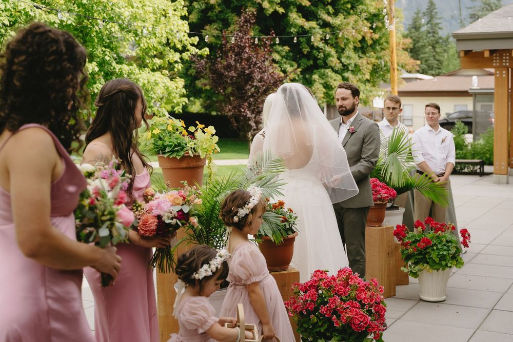 Wedding party in pink dresses poses in a lush garden setting with colorful floral arrangements.