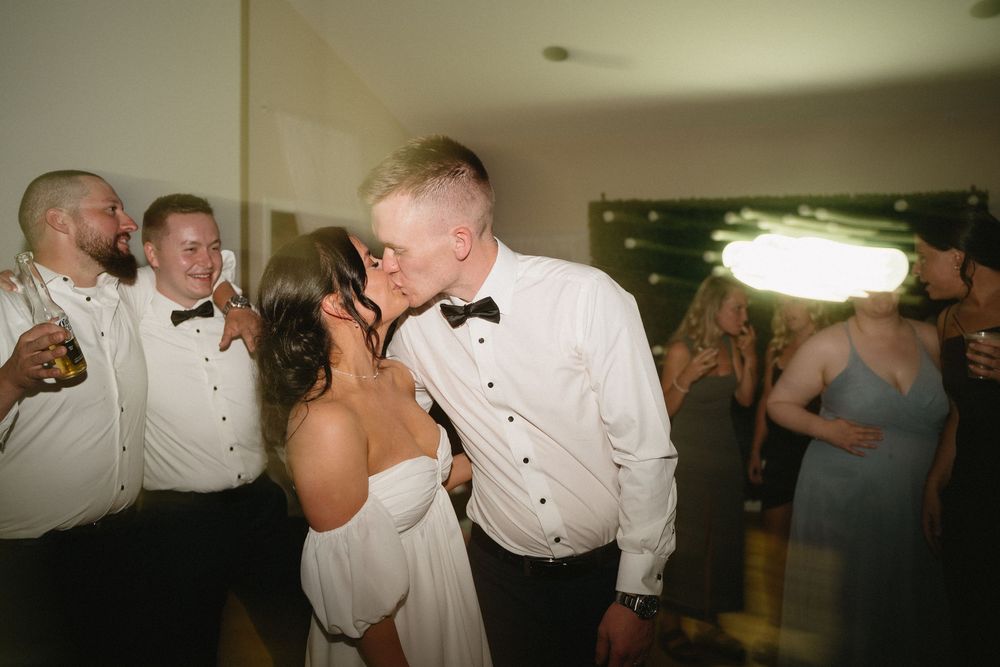 Wedding guests in white shirts and bow ties dance and celebrate together on the dance floor at a reception.