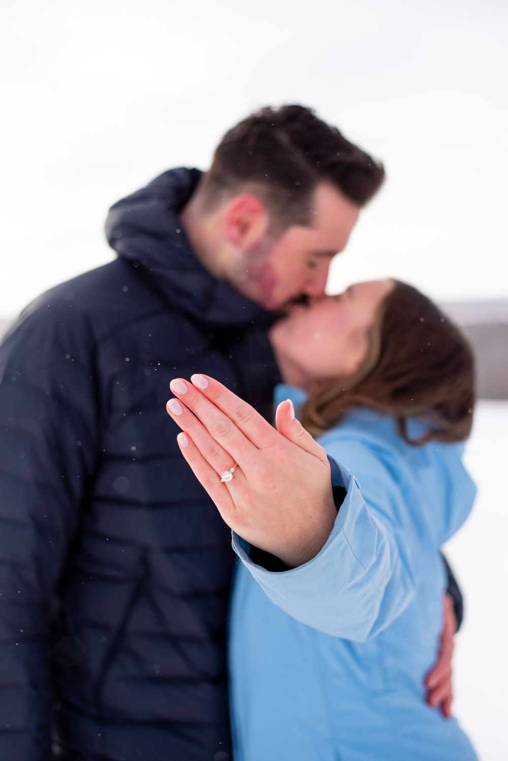A romantic proposal moment in the snow with a diamond ring prominently displayed.