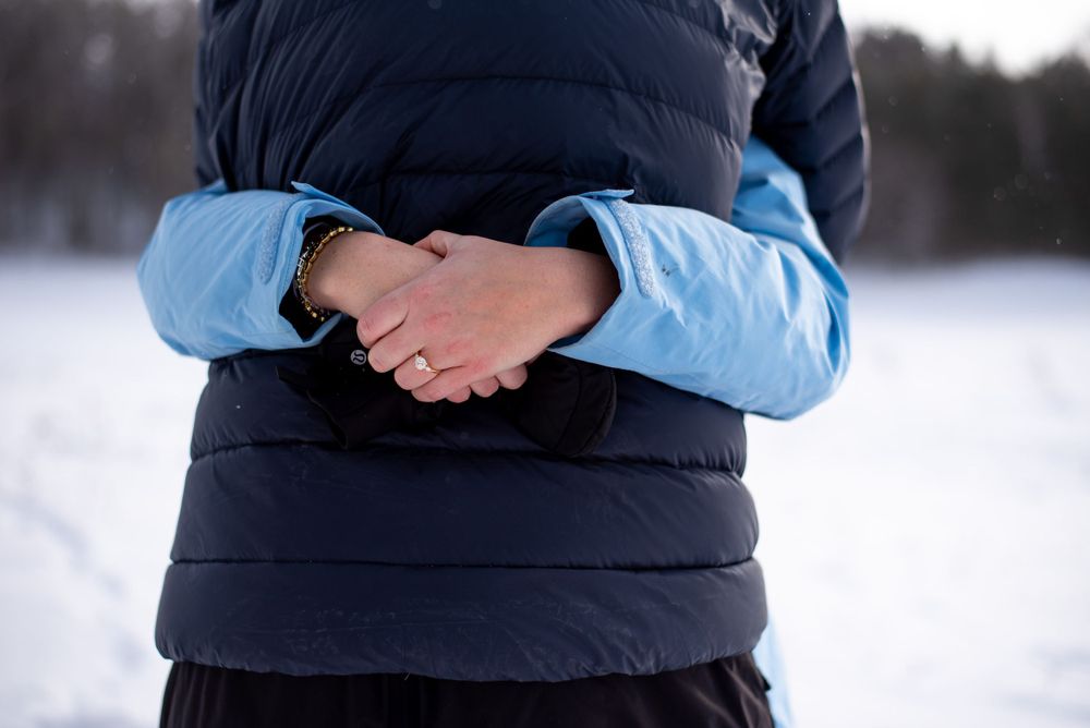 Two people in winter coats embrace in a close hug against a snowy landscape background.