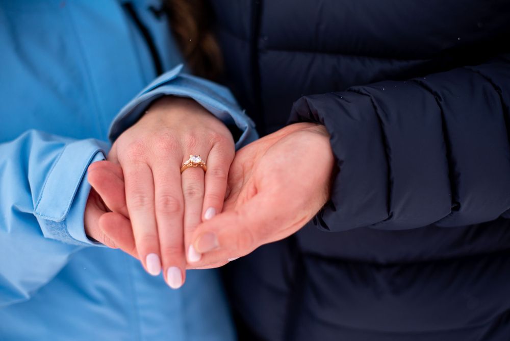 Close-up of hands showing an engagement ring against winter coats.
