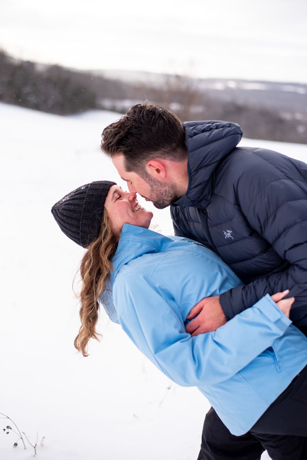 A romantic winter embrace captured against a snowy landscape background.