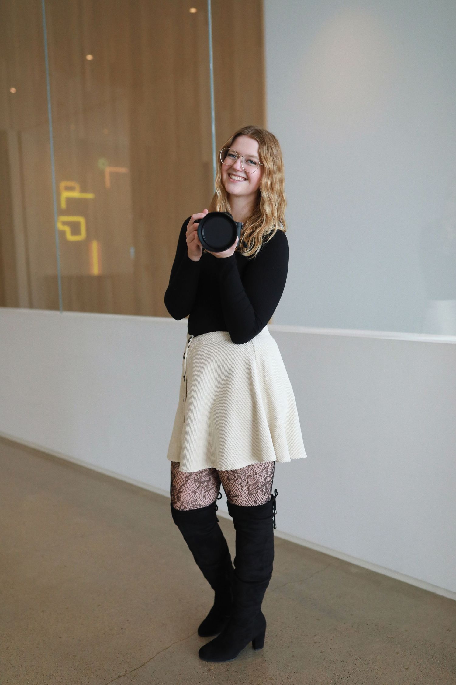 Fashion model in black and cream outfit poses with camera against neutral studio background.