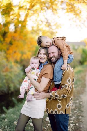 Family and their brown dog pose together for autumn photos in a park with golden foliage in the background.